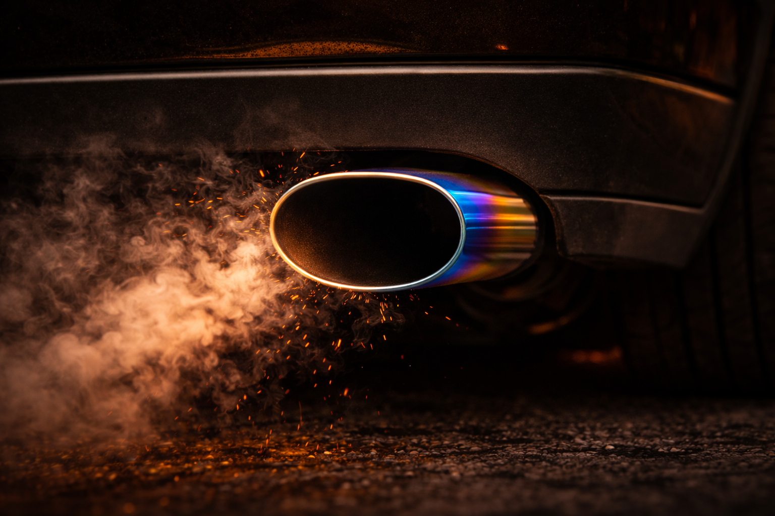 Car exhaust pipe emitting smoke and glowing embers in low light.